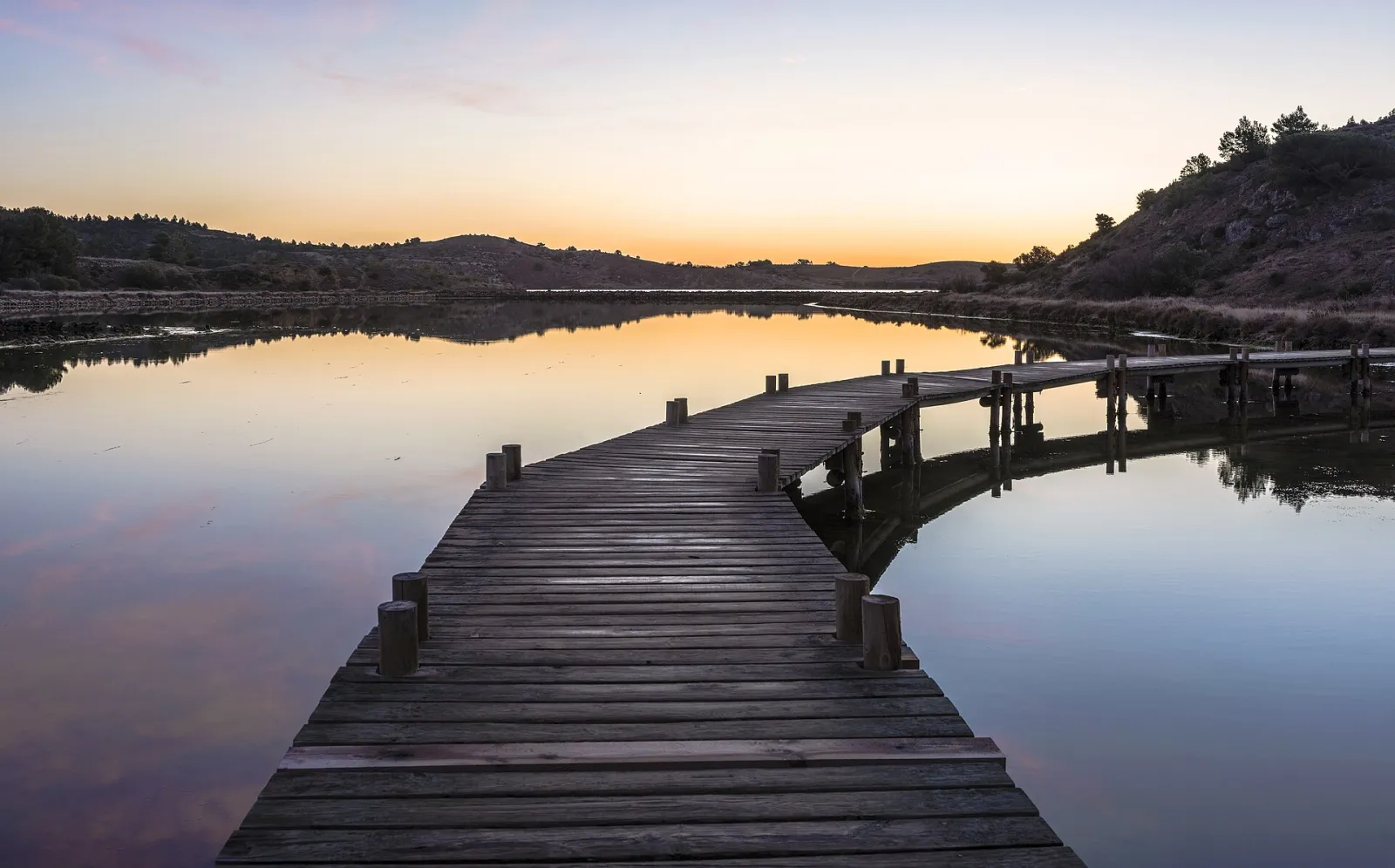Hills, trees and a footbridge reflected in the former salt ponds of Peyriac-de-Mer in Aude, southern France