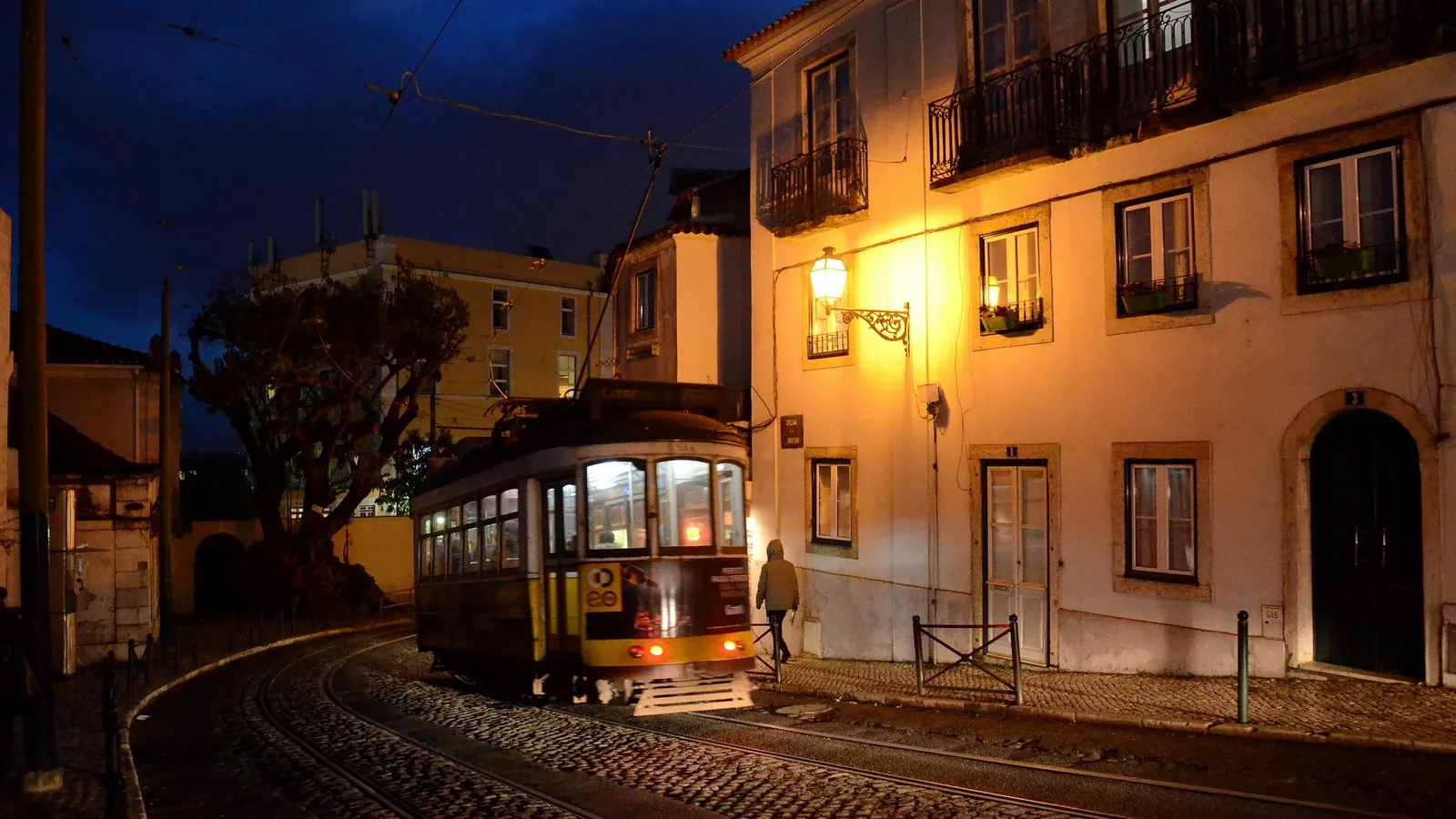 A yellow Lisbon tram on route 28 rounding a corner in the old town at dusk